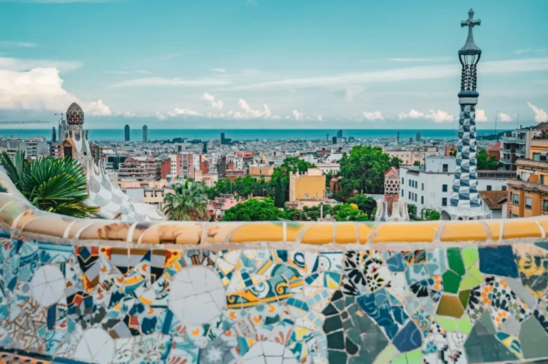 View across Barcelona from Park Güell, with colourful mosaic tiles in the foreground and the city stretching to the sea