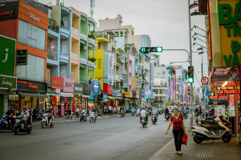 A busy street in Ho Chi Minh City lined with colourful shophouses, motorbikes, and pedestrians