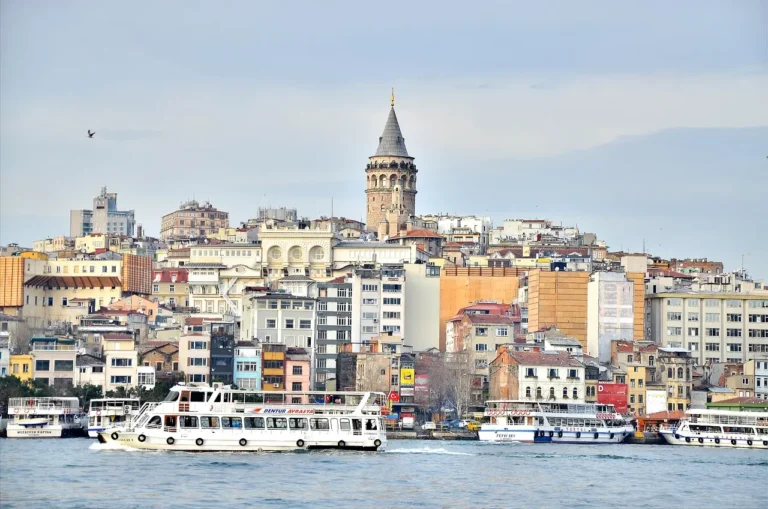 Galata Tower above the rooftops of Beyoglu, with passenger ferries crossing the Golden Horn in the foreground.