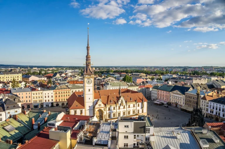 View across Olomouc's Upper Square, with the town hall clock tower and the baroque Holy Trinity Column among the terracotta rooftops.
