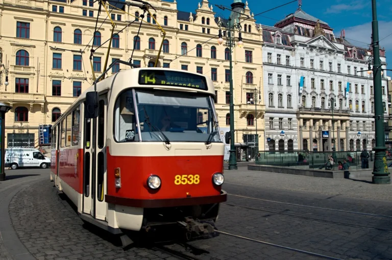 A red and cream Prague tram rounding a bend past grand historic buildings in the city centre.